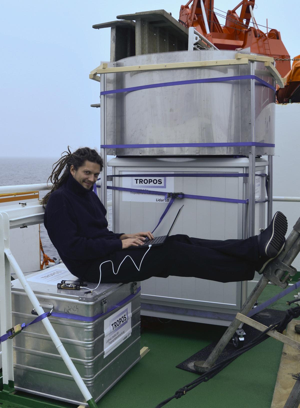 Hannes Griesche vom TROPOS vor dem Wolkenradar. In dem Schrank befindet sich eine Stabilisierungsplattform, welche die Schiffsbewegungen ausgleicht, so dass das Radar jederzeit senkrecht in den Himmel schaut. Foto: Carola Barrientos, TROPOS